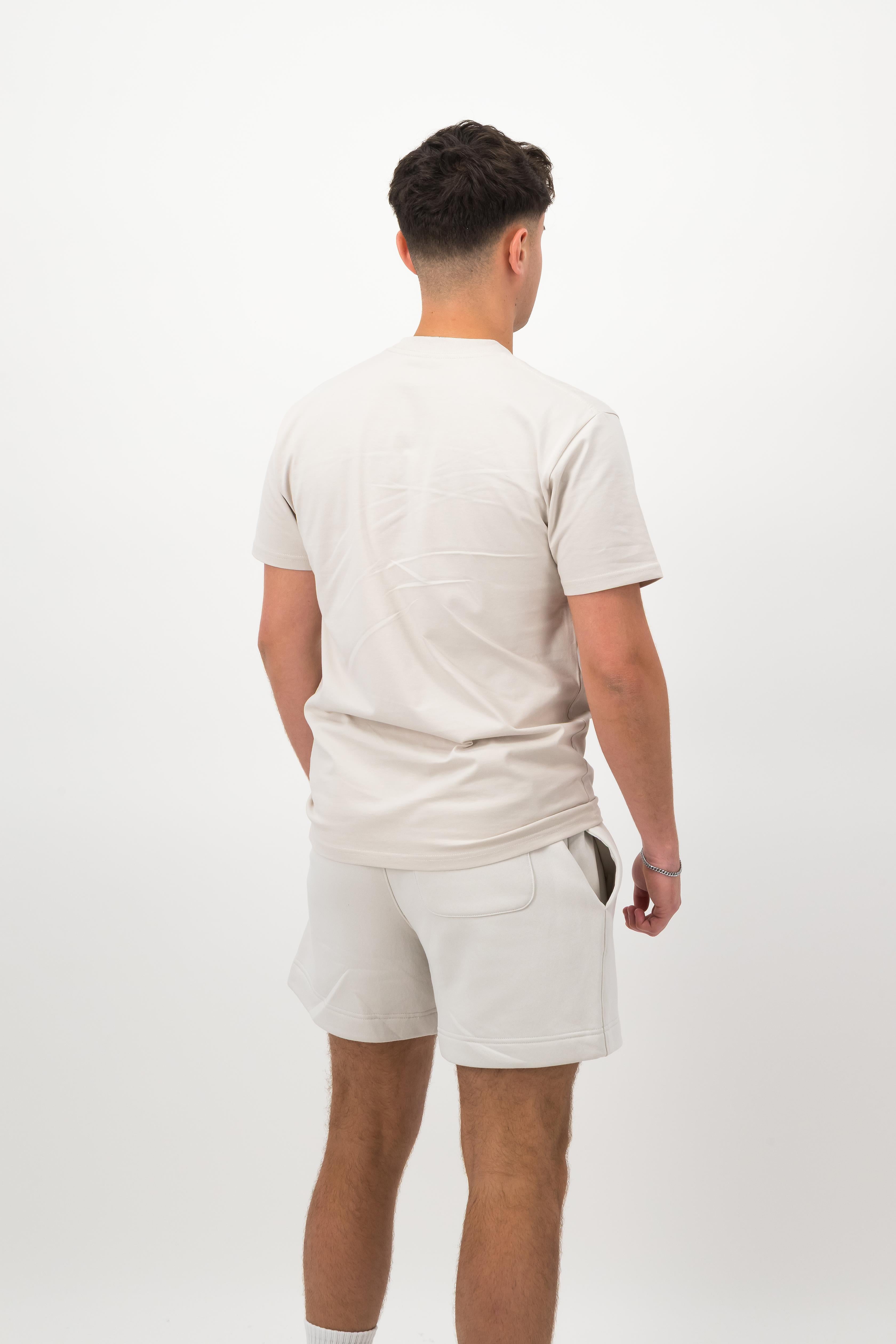 Person wearing a Concept Padel bone rebound tee standing with back to camera showing the clean back silhouette, styled with white shorts and trainers against a white background
