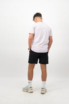 Person wearing a Concept Padel orchid rebound tee standing with back to camera showing the clean back silhouette, styled with black shorts and trainers against a white background