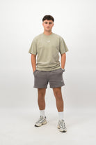 Person wearing a Concept Padel eucalyptus faded tee standing facing forward, styled with grey shorts and trainers against a white background