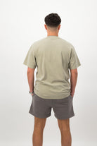 Person wearing a Concept Padel eucalyptus faded tee standing with back to camera showing the clean back silhouette, styled with grey shorts and trainers against a white background