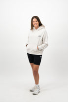 Woman wearing a Concept Padel bone serve hoodie standing facing forward, styled with black shorts and trainers against a white background