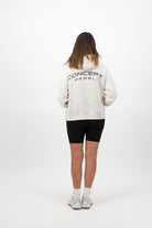 Woman wearing a Concept Padel bone serve hoodie standing with back to camera showing the back arch logo, styled with black shorts and trainers against a white background
