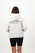 Woman wearing a Concept Padel bone serve hoodie standing with back to camera showing the back arch logo, styled with black shorts and trainers against a white background