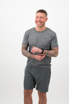 Person wearing a Concept Padel graphite performance tee standing side on, paired with dark shorts and trainers against a white background