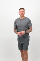 Person wearing a Concept Padel graphite performance tee standing facing forward, styled with dark shorts and trainers against a white background