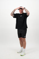 Person wearing a black T‑shirt, black shorts and a black cap with hands on head against a white background