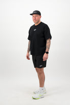Side view of a person wearing a black T‑shirt, black shorts and a black cap against a white background