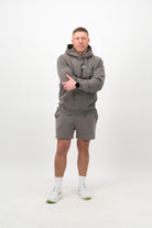 Person wearing a Concept Padel grey faded hoodie standing facing forward, styled with grey shorts and trainers against a white background