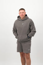 Person wearing a Concept Padel grey faded hoodie standing facing forward, styled with grey shorts and trainers against a white background