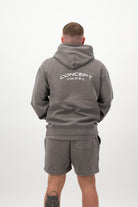Person wearing a Concept Padel grey faded hoodie standing with back to camera showing the back branding, styled with grey shorts and trainers against a white background