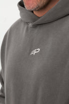 Close‑up of the embroidered Concept Padel logo on the grey faded hoodie worn against a white background