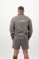 Person wearing a Concept Padel grey faded 1/4 zip sweatshirt standing with back to camera showing the back branding, styled with grey shorts and trainers against a white background