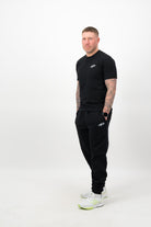 Person wearing a Concept Padel black rebound tee standing side on, paired with black joggers and trainers against a white background