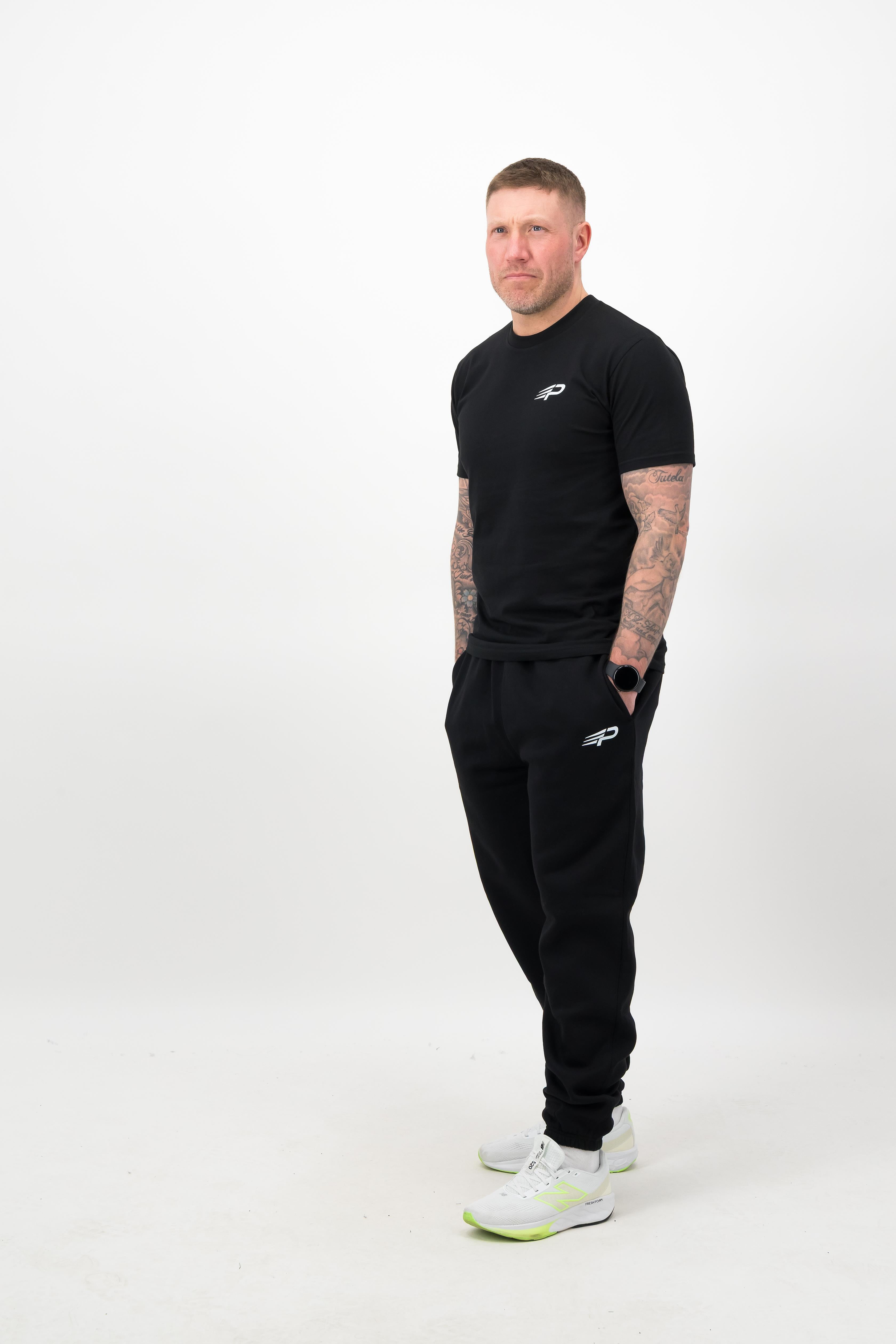 Person wearing a Concept Padel black rebound tee standing side on, paired with black joggers and trainers against a white background