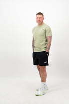 Person wearing a Concept Padel pistachio rebound tee standing facing forward, styled with black shorts and trainers against a white background