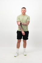Person wearing a Concept Padel pistachio rebound tee standing facing forward, styled with black shorts and trainers against a white background