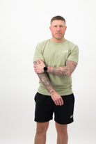 Person wearing a Concept Padel pistachio rebound tee standing facing forward, styled with black shorts and trainers against a white background