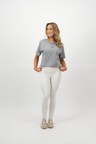 Woman wearing a Concept Padel storm court tee standing side on with one arm slightly bent, paired with black shorts and trainers against a white background