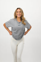 Woman wearing a Concept Padel storm court tee standing in a relaxed pose with weight shifted to one leg, paired with black shorts and trainers against a white background