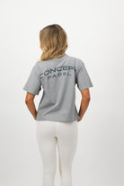 Woman wearing a Concept Padel storm court tee standing with back to camera showing the relaxed silhouette, styled with black shorts and trainers against a white background