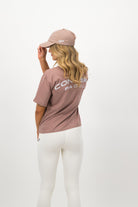 Back view of woman wearing hazy pink Concept Padel cap with white leggings