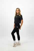 Woman wearing a Concept Padel black faded crop tee standing side on, paired with black leggings and trainers against a white background