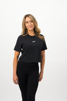 Woman wearing a Concept Padel black faded crop tee standing facing forward, styled with black leggings and trainers against a white background