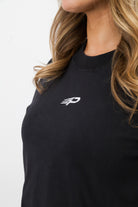 Close‑up of the embroidered Concept Padel logo on the black faded crop tee worn by a woman against a white background