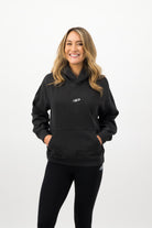 Woman wearing a Concept Padel black faded hoodie standing facing forward, styled with black leggings and trainers against a white background