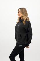 Woman wearing a Concept Padel black faded hoodie standing side on, paired with black leggings and trainers against a white background