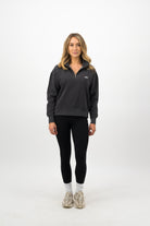 Woman wearing a Concept Padel black faded 1/4 zip sweatshirt standing facing forward, styled with black leggings and trainers against a white background