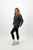 Woman wearing a Concept Padel black faded 1/4 zip sweatshirt standing side on, paired with black leggings and trainers against a white background