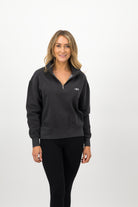 Woman wearing a Concept Padel black faded 1/4 zip sweatshirt standing facing forward, styled with black leggings and trainers against a white background